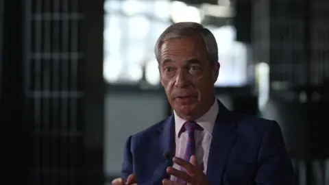 BBC Nigel Farage, dressed in a dark suit and tie, stares intently at the camera