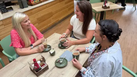 Three members of Sisters in Service are chatting over drinks in a cafe
