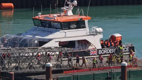PA Media A group of people thought to be migrants are brought in to the Border Force compound in Dover, Kent, from a Border Force vessel following a small boat incident in the Channel on 9 September. The people getting off the boat are wearing life jackets. 