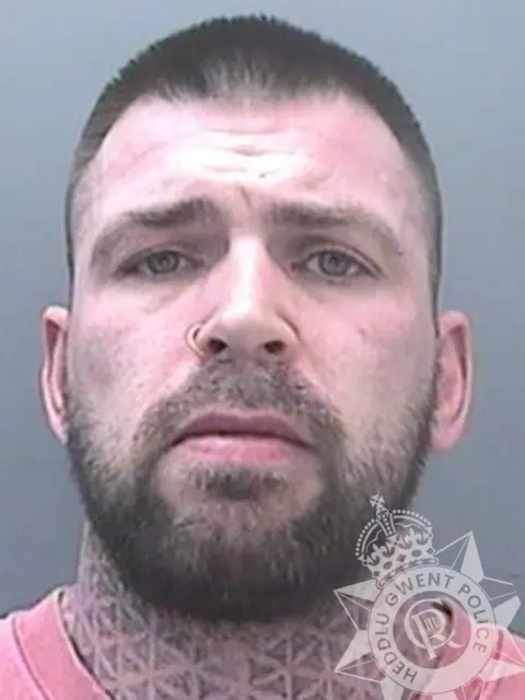 Gwent Police A police mugshot of a white hit-and-run driver with a beard and short brown hair with a tattoo on his neck