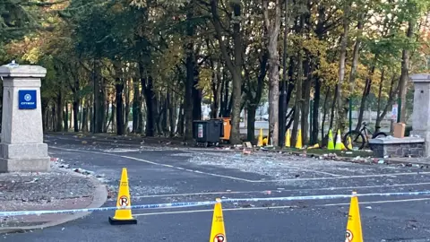 a number of yellow cones are placed outside the entrance to a hotel where violence had broke out earlier - debris can be seen on the surface of the road
