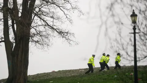 PA Media Image from January 2024 showing four uniformed police officers walking across Primrose Hill after the fatal attack, with a lamp post and tree visible in the foreground