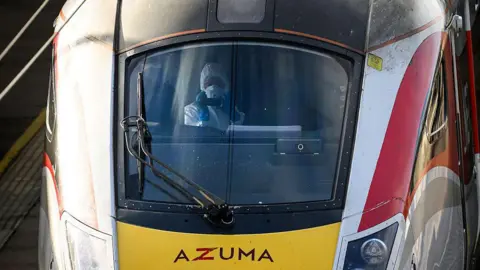 Getty Images A forensics officer sits in the train driver's seat. They are wearing a protective white cover-all and a white face mask holds a camera up.
