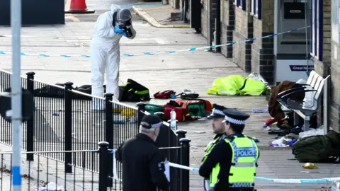 Reuters A forensics officer in a white protective suit photographs object strewn on the floor of the train station. Some police officers are stood nearby. The area is cordoned off.