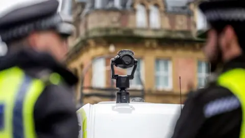 PA Media Police officers stand behind a van with a facial recognition camera on its roof