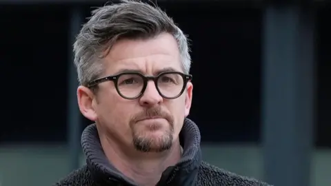 PA Media Joey Barton with grey hair and brown beard and black glasses wearing a grey hoodie.