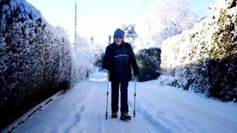 Carl Recine/Getty Images A woman walks through a snowy lane wearing a wooly hat, using poles.