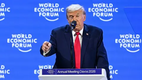 Getty Images Donald Trump delivers a speech from a lectern at the World Economic Forum in Davos wearing a navy suit, red tie and a US flag pinned to his suit.