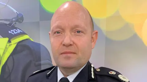 PA Media Chief Constable Craig Guildford, of West Midlands Police, at the police headquarters in Birmingham. He is bald and wearing a police uniform in front of a grey and yellow backdrop.